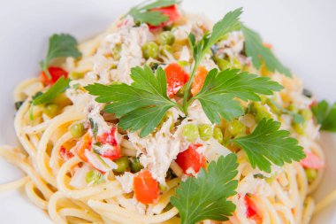 Krema soslu spagetti tütsülenmiş uskumru, bezelye, dolma biber ve beyaz bir tabakta maydanoz.