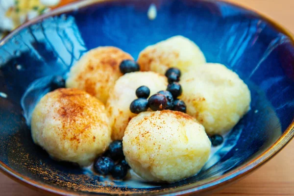 Six homemade sweet dumplings served with vanilla cream and blueberries in blue ceramic vintage bowl