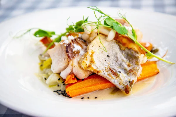 Delicious fillet of cod fish with carrots, leeks and mushrooms in white plate ready to be served