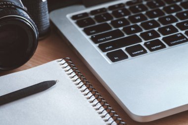 Ahşap ofis resepsiyon masası defter, kalem, retro kamera ve bilgisayar ile. Üstten görünüm. Parlak nokta mavi tonda. Düşük anahtar atış.