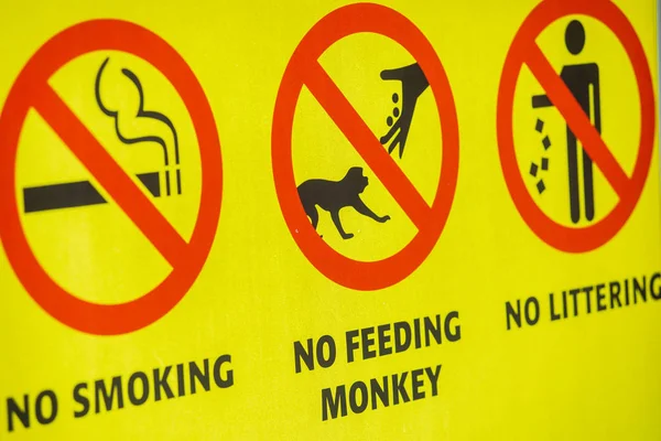 Yellow sign that says no smoking no feeding monkeys no littering