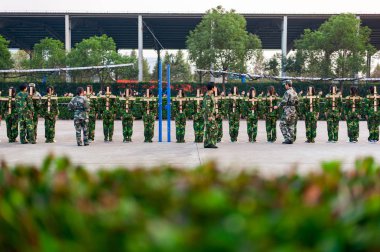SHAOXING, CHINA - NOVEMBER 06 2012: Chinese freshmen college students are sitting still during military training at school. view from the back clipart