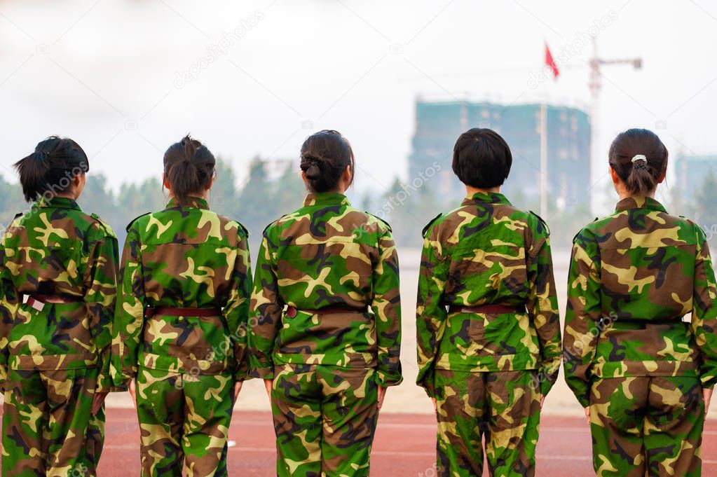 Chinese freshmen college students are standing stand still during military training at school. view from the back