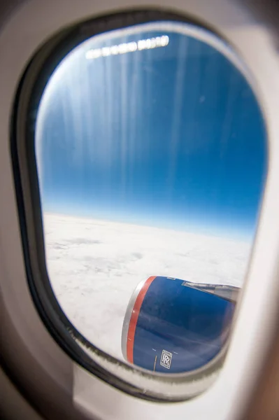 Plane window view with blue sky and clouds and aircraft engine trough the plane porthole