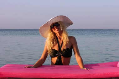 Sarışın kız pembe şişme şişme Kızıldeniz su beyaz şapka ve güneş gözlüğü yalan