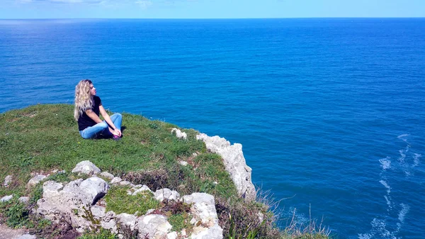 Chica rubia sentada en la roca, mirando el agua — Foto de Stock