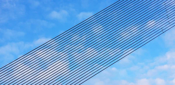 Black metal line rows against a blue sky with white clouds. Background of parallel lines arranged in perspective in an inclined plane. Designer materials. Modern geometric construstion.