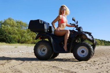 uzun sarı saçlı bikini çekici kadın dört bisiklet, güneşli bir gün oturuyor.