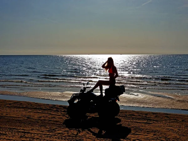 Silueta de una mujer con el pelo largo y rubio sentado en una quad bike, día soleado en la playa . — Foto de Stock