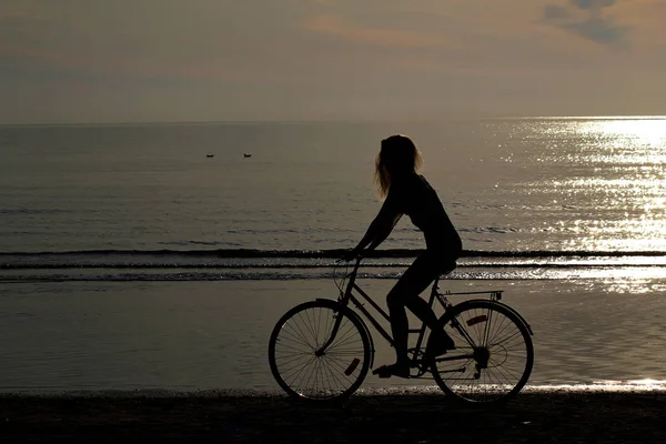 一个长发的女孩骑着自行车在波罗的海的沙上。拍摄太阳. — 图库照片