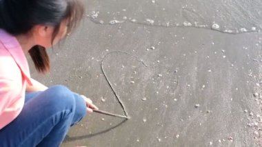 Kız plajda kalp şekli çizim