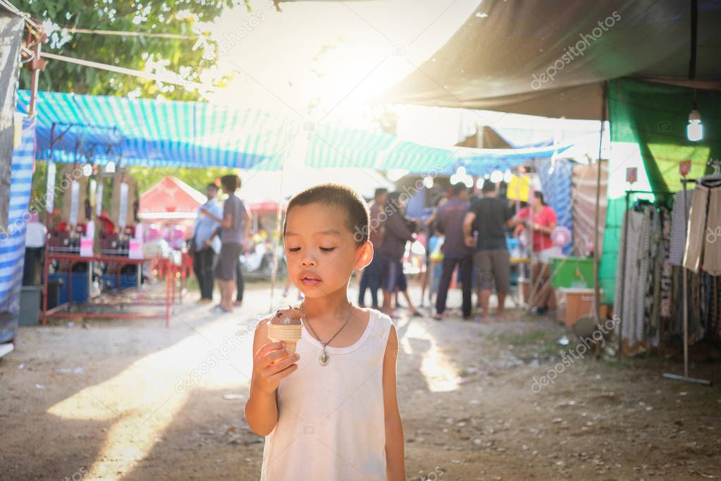 Little boy enjoy eating chocolate ice-cream cone while walking in the market