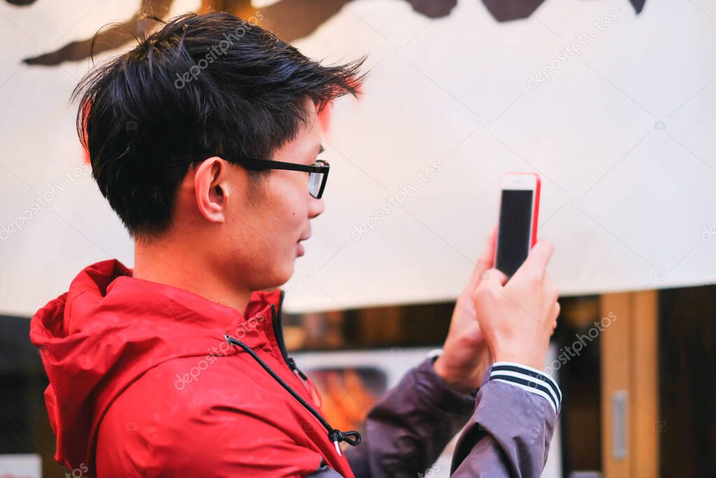 Side view of young asian man unlocking smartphone with facial recognition and touching fingerprint while using phone for video call and chatting with friend concept 
