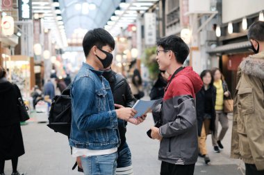 Bir grup Asyalı genç arkadaş trafiğin yoğun olduğu saatlerde yürüyüş gezisi hakkında konuşmayı keser.