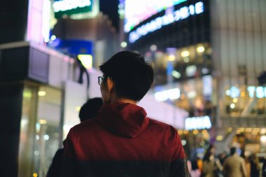 Gece vakti Bokeh Light arka planıyla büyük şehirdeki mağazanın önünde yürüyen genç adam.