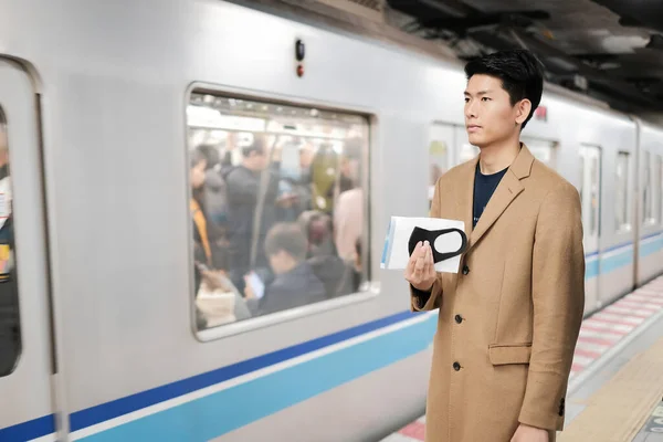 Asian man holding surgical face mask and map to protect covid-19 virus while waiting for the train and go to next station