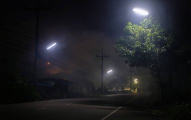 Gece dumanlı sokak lambalarının altındaki boş yol ve arka planda UFO