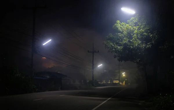 Gece dumanlı sokak lambalarının altındaki boş yol ve arka planda UFO