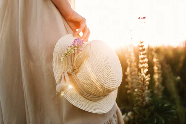 Donna in possesso di cappello di paglia con un nastro su sfondo campo di fiori. fasci di luce calda tramonto — Foto Stock