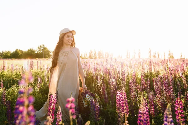 Bella giovane donna in abito bianco e cappello di paglia passeggiando nel campo di fiori — Foto Stock