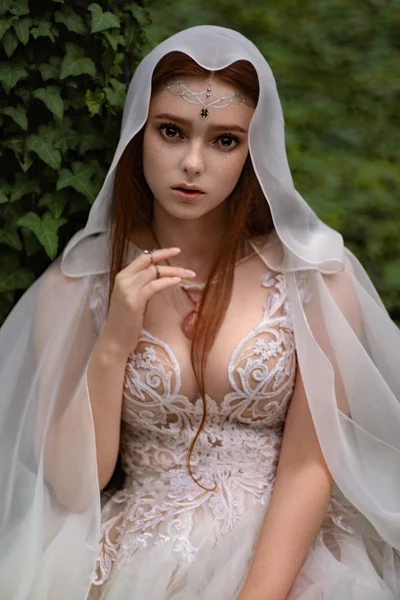 緑の庭でポーズ白いドレスとケープで魅力的なジンジャーエルフの女性 — ストック写真