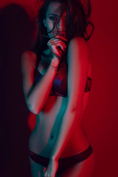 暗い赤いスタジオの背景にポーズランジェリーで魅惑的なブルネットモデル — ストック写真