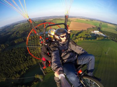 Powered paragliding tandem flight, man taking selfie with action camera clipart
