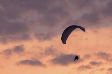 Akşam vakti gökyüzünden düşen paraşütçü. Dramatik bir gökyüzü. Eğlence sporu, renkli gökyüzünde paraşütçü silueti.