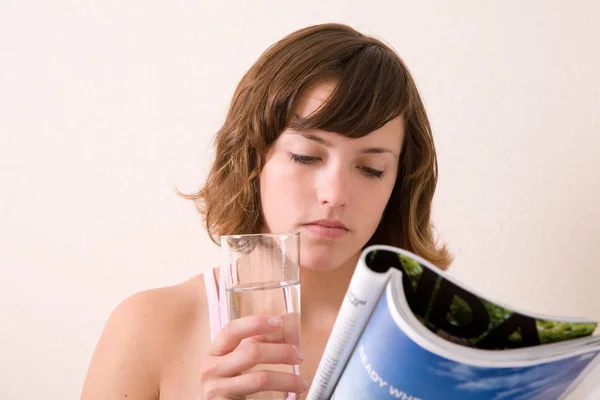 Όμορφη Μελαχρινή Διαβάζει Ένα Περιοδικό Και Πίνει Ένα Ποτήρι Νερό — Φωτογραφία Αρχείου