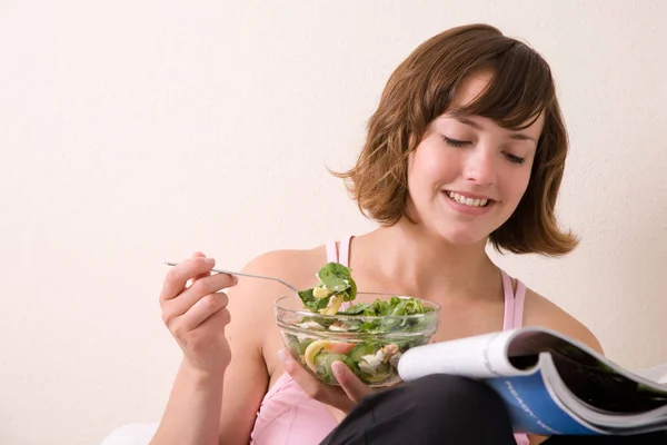 Bonita Morena Leyendo Una Revista Sofá Mientras Come Una Ensalada — Foto de Stock