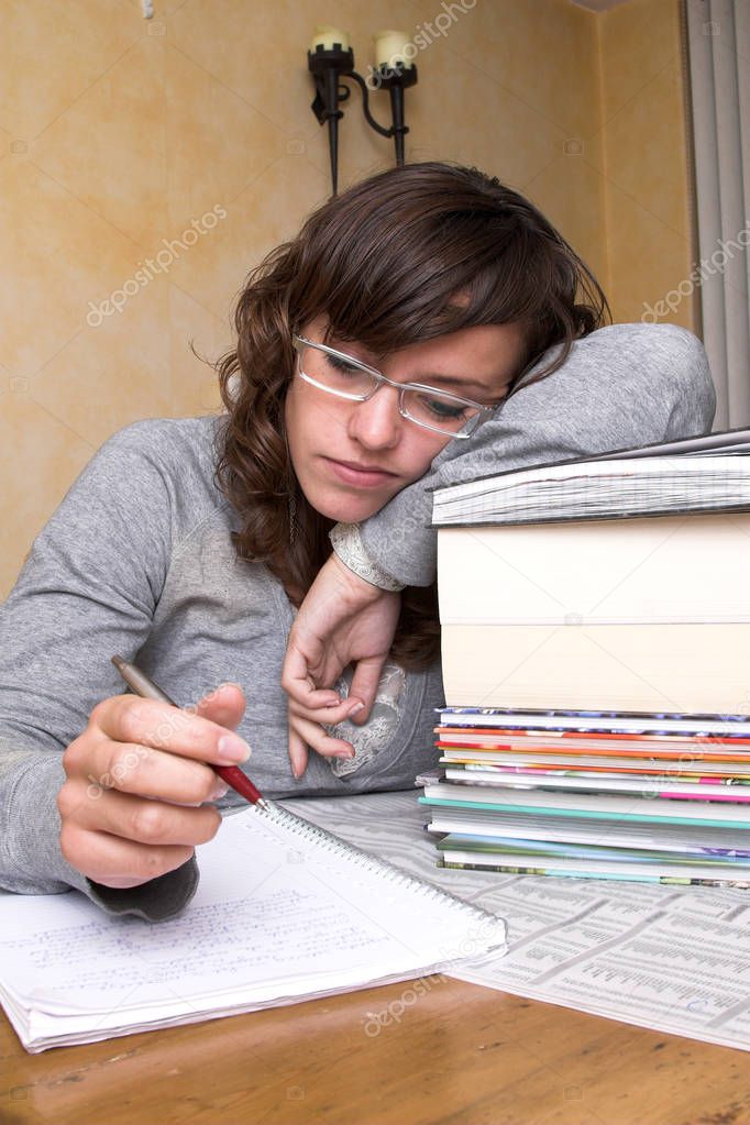 Tired student leaning over her books still looking at her notes