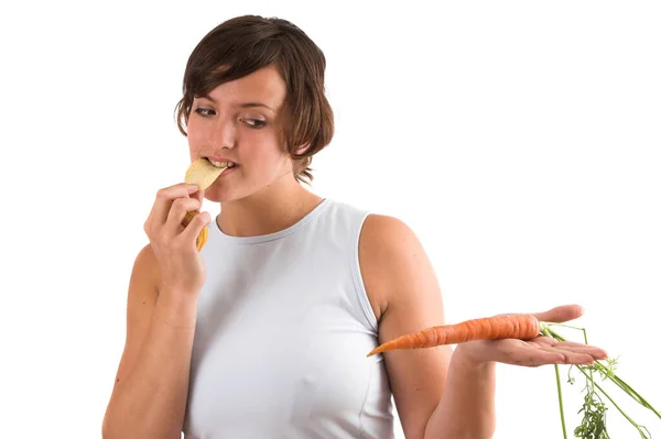 漂亮的黑发姑娘一边吃着薯片一边内疚地看着手中那只健康得多的胡萝卜 — 图库照片