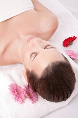 Güzel, beyaz bir kadın spa merkezinde uzanıyor. Rahatlıyor, çiçekler etrafında. 
