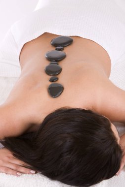 Masaj masasına uzanmış sıcak taş masajı yaptıran bir kadın.