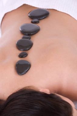 Sırtında sıcak taşlarla masaj masasında yatan bir kadın.