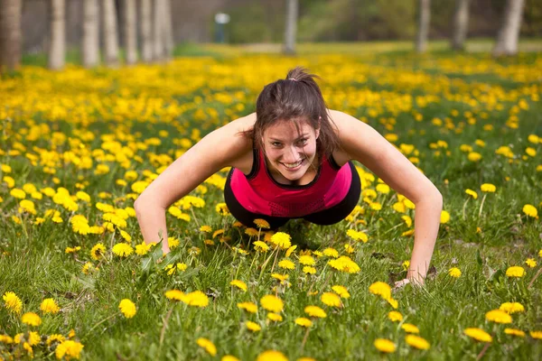一个活泼的黑发女人在户外 用黄色的花朵在田野里做俯卧撑 微笑着看着相机 — 图库照片