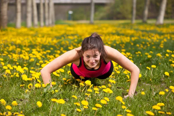 一个活泼的黑发女人在户外 用黄色的花朵在田野里做俯卧撑 微笑着看着相机 免版税图库图片