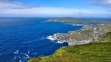 Batı İrlanda Sahil panoramik manzaralı. Ön planda uçuruma kayalar, kuşlar, çim, inek, dalgalar, sprey ile görebilirsiniz. Arka planda bulutlar ve martılar denize sıfır olduğunu.