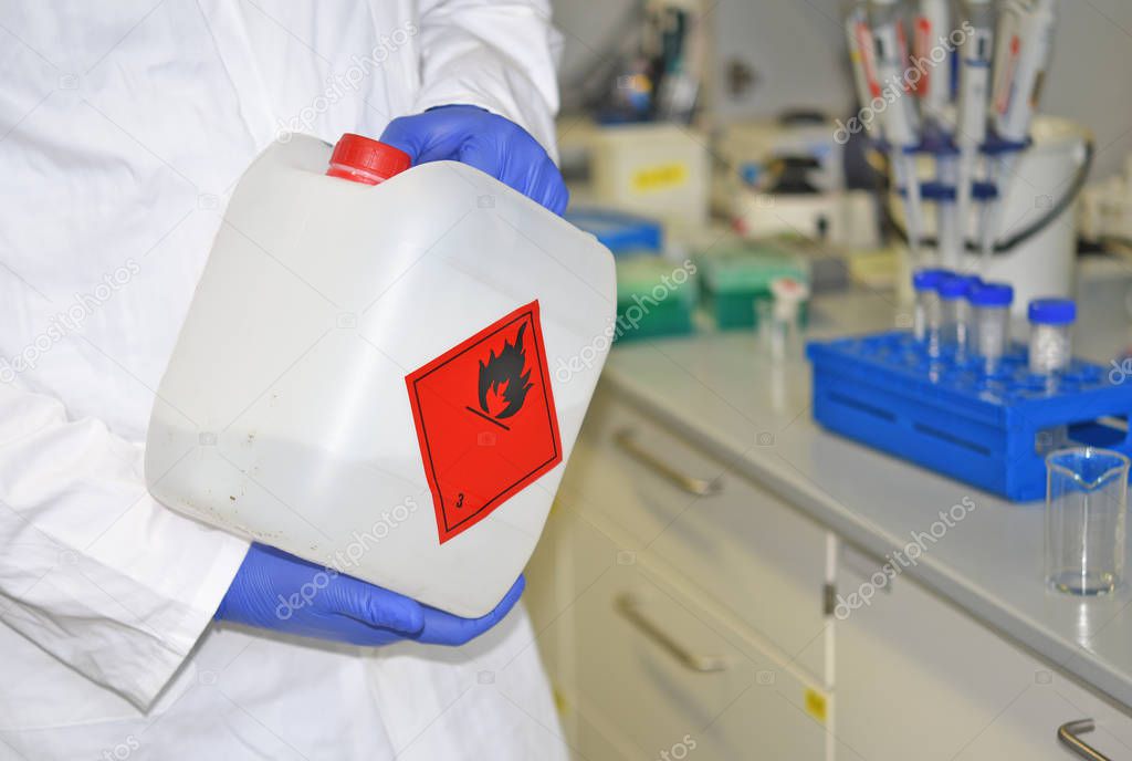 An employee at a biochemical laboratory works with flammable liquid in a plastic canister with appropriate marking near the working surface in the laboratory.