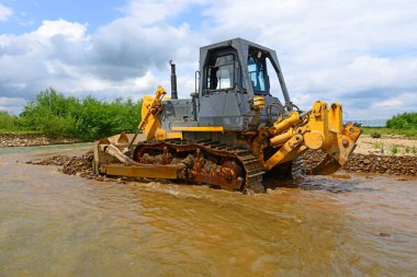 The bulldozer performs works in the tideway of mountain small river