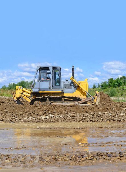 The bulldozer performs works in the tideway of mountain small river