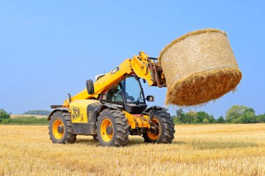 Kalush, Ukraine - August 13: Universal loader harvesting straw in the field near the town Kalush, Western Ukraine August 13, 2015 clipart