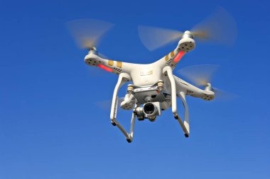 Mavi gökyüzünde uçan İHA arka planda 