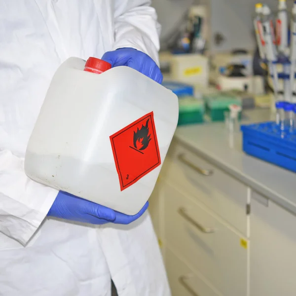 生化实验室的一名员工在实验室工作表面附近的塑料罐中使用易燃液体 并在实验室的工作表面附近打上适当的标记 图库照片