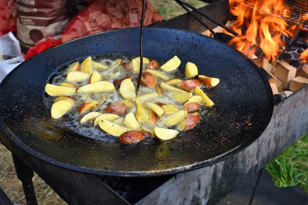 Cooking potatoes in a flat pan with sunflower oil on an open fire of the chargrill. Street trade on a city holiday.