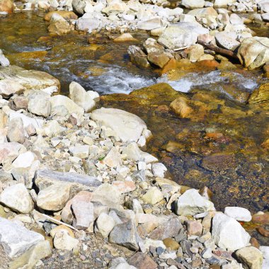 waterfall on river in autumn day with rocks and small stones in the background