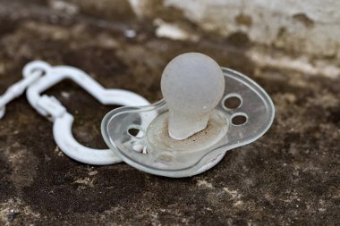 dirty silicone pacifier lying on the ground. clipart