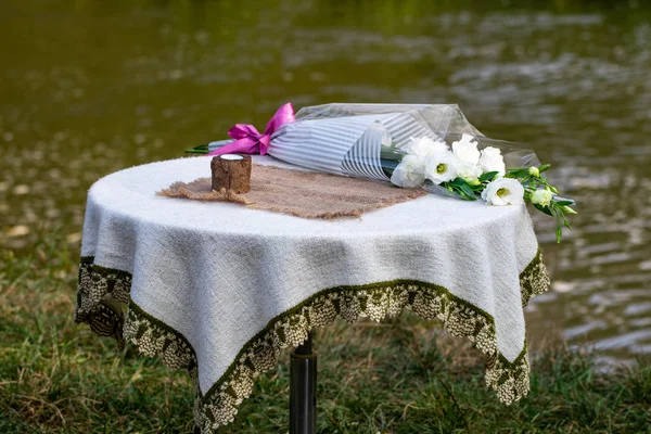 candle and a bouquet of flowers are on the table against the river. The concept of baptism.