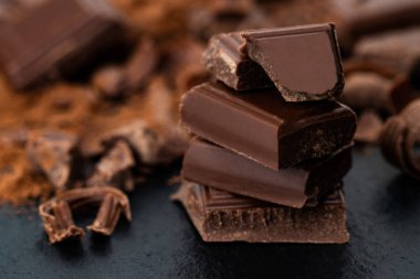 Kırık çikolata parçaları ve karanlık bir arka plan üzerine kakao tozu.