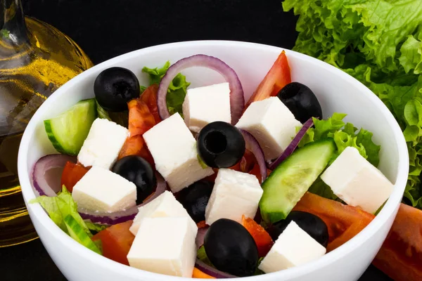 Greek salad with fresh vegetables, feta cheese and black olives on a dark background.